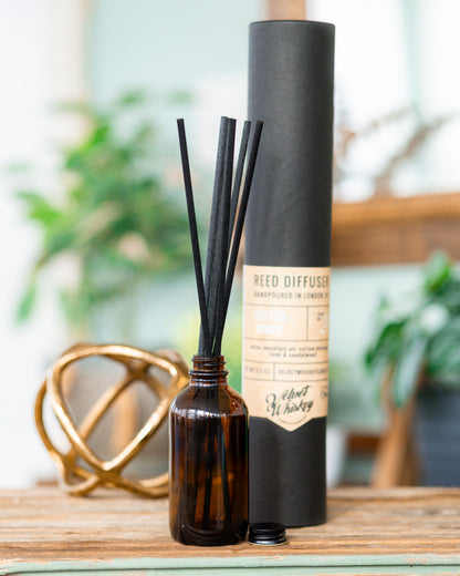 An amber bottle with black fiber reed diffuser reeds sitting on a table.